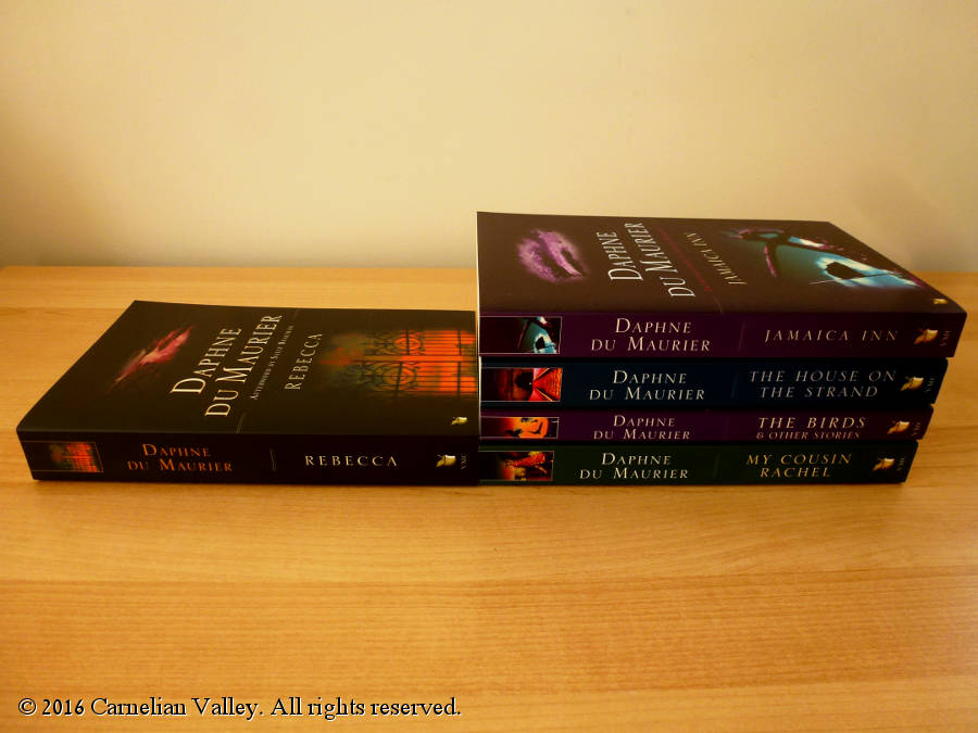 A photograph of Daphne Du Maurier books - four in one pile, Rebecca standing alone as the only book I've read so far