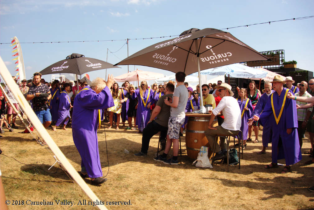 A photograph of a choir in robes singing amongst the crowd in the bar area