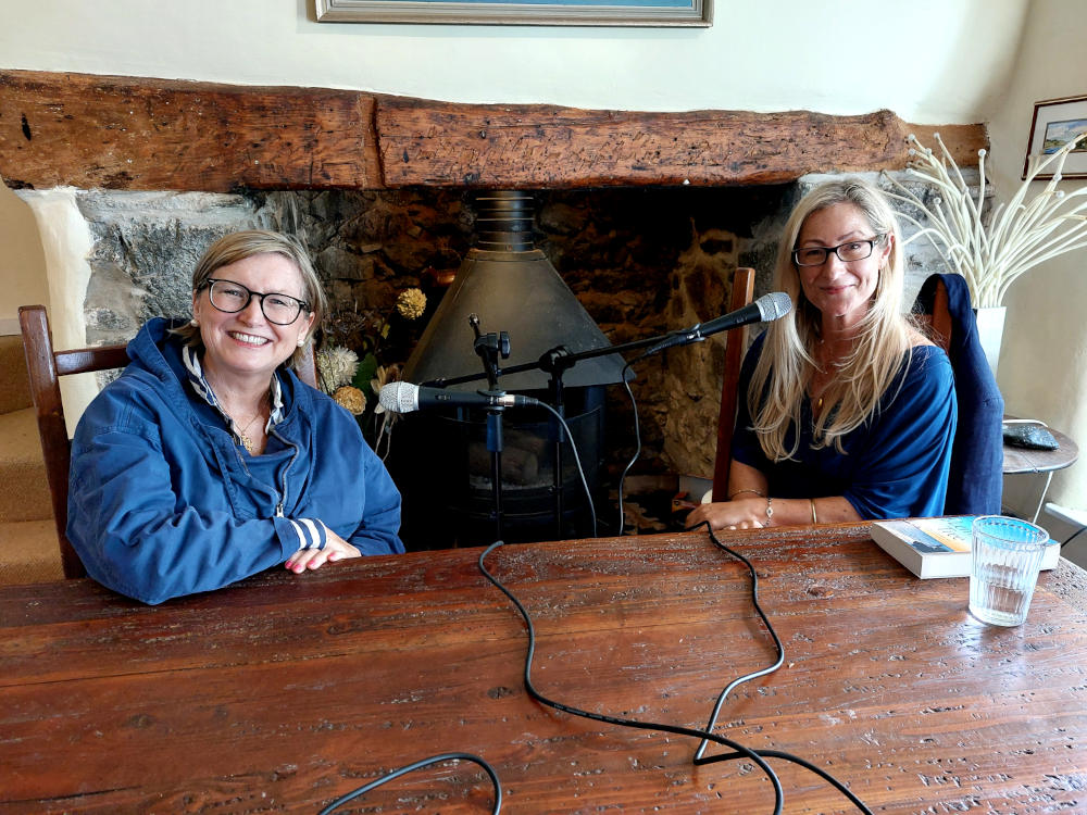 A photo of Liz Fenwick and Emma Cowell sat at a table for a podcast recording with recording equipment around them