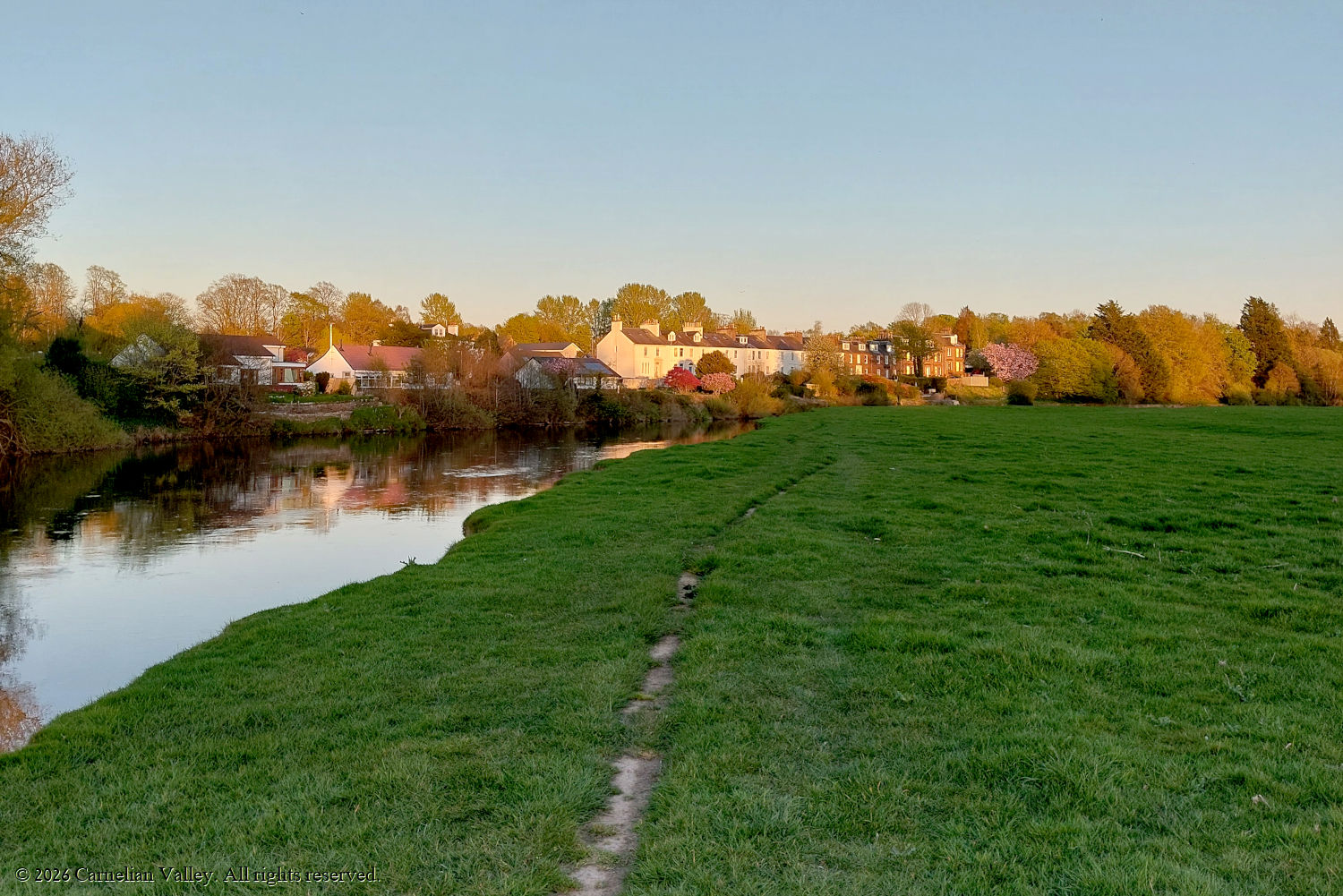 A photo of a field at sunset in April, a river inbetween the photographer and countryside houses